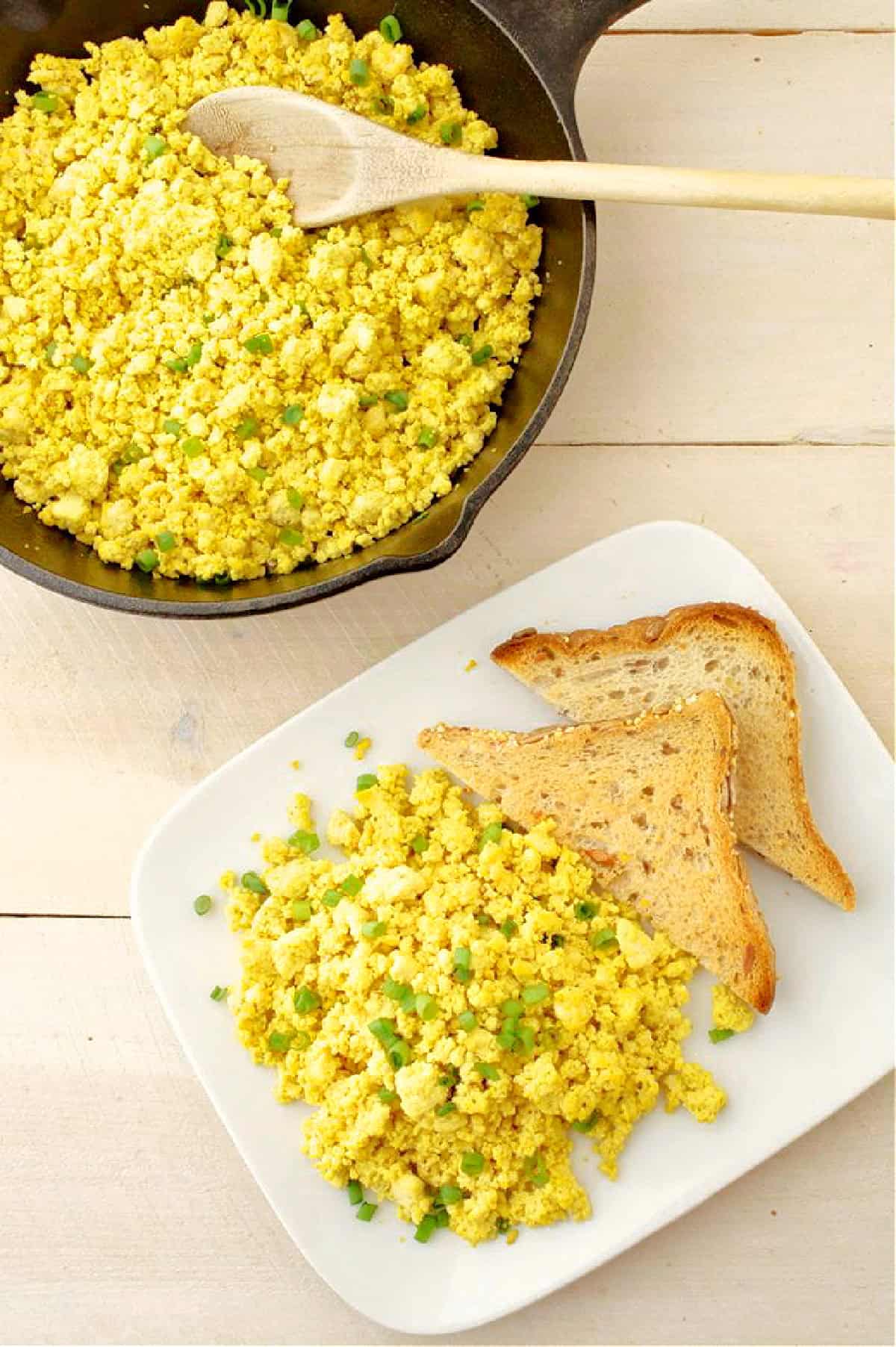 Tofu scramble and toast on a white plate with a skillet of tofu scramble.