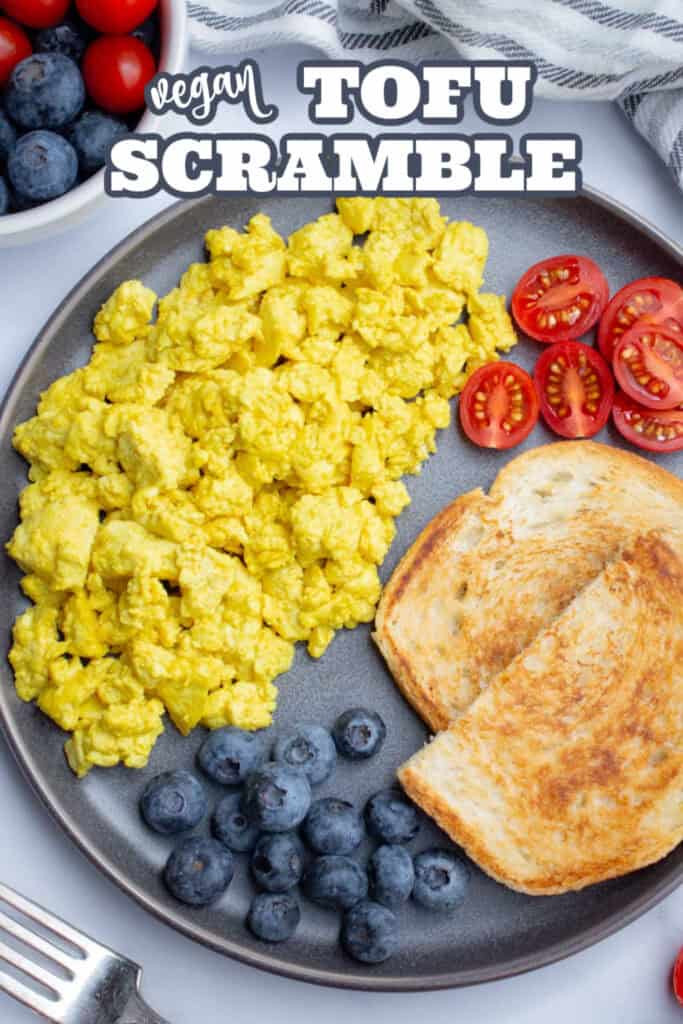A plate of tofu scramble, toast, blueberries, and cut cherry tomatoes with overlay text "Vegan Tofu Scramble."