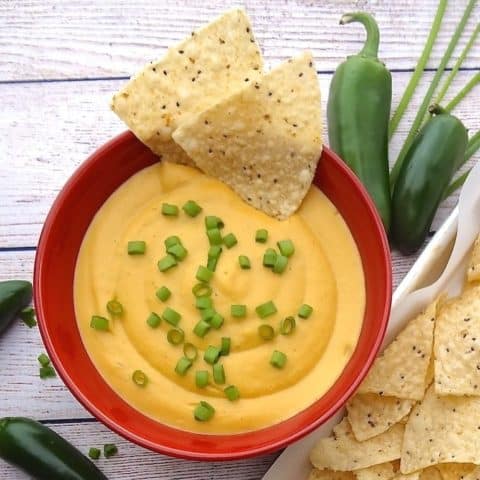 vegan nacho cheese in a red bowl with tortilla chips.