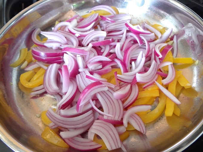A frying pan with sliced red onion and yellow bell peppers ready to be sautéed. 