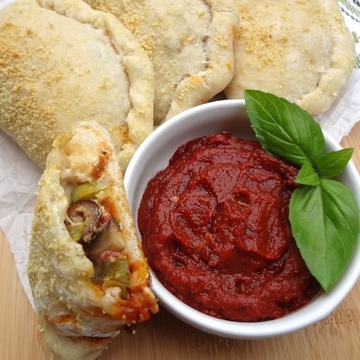 Half of a vegan pizza pocket with a side of marinara for dipping.