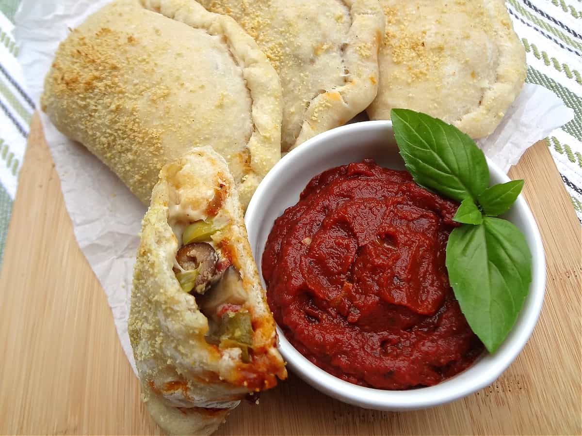 Half of a vegan pizza pocket with a side of marinara for dipping.