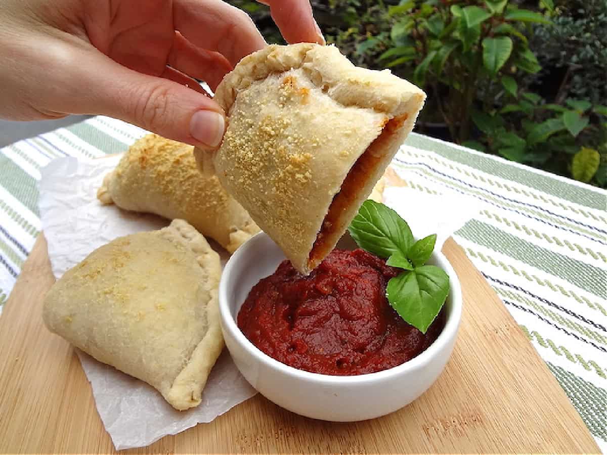 Half of a vegan pizza pocket dipping into marinara sauce.