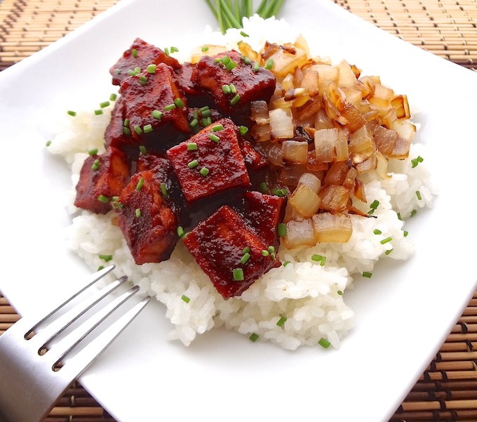 Plated white organic sushi rice topped with diced caramelized onions and oven baked bbq tofu slices.