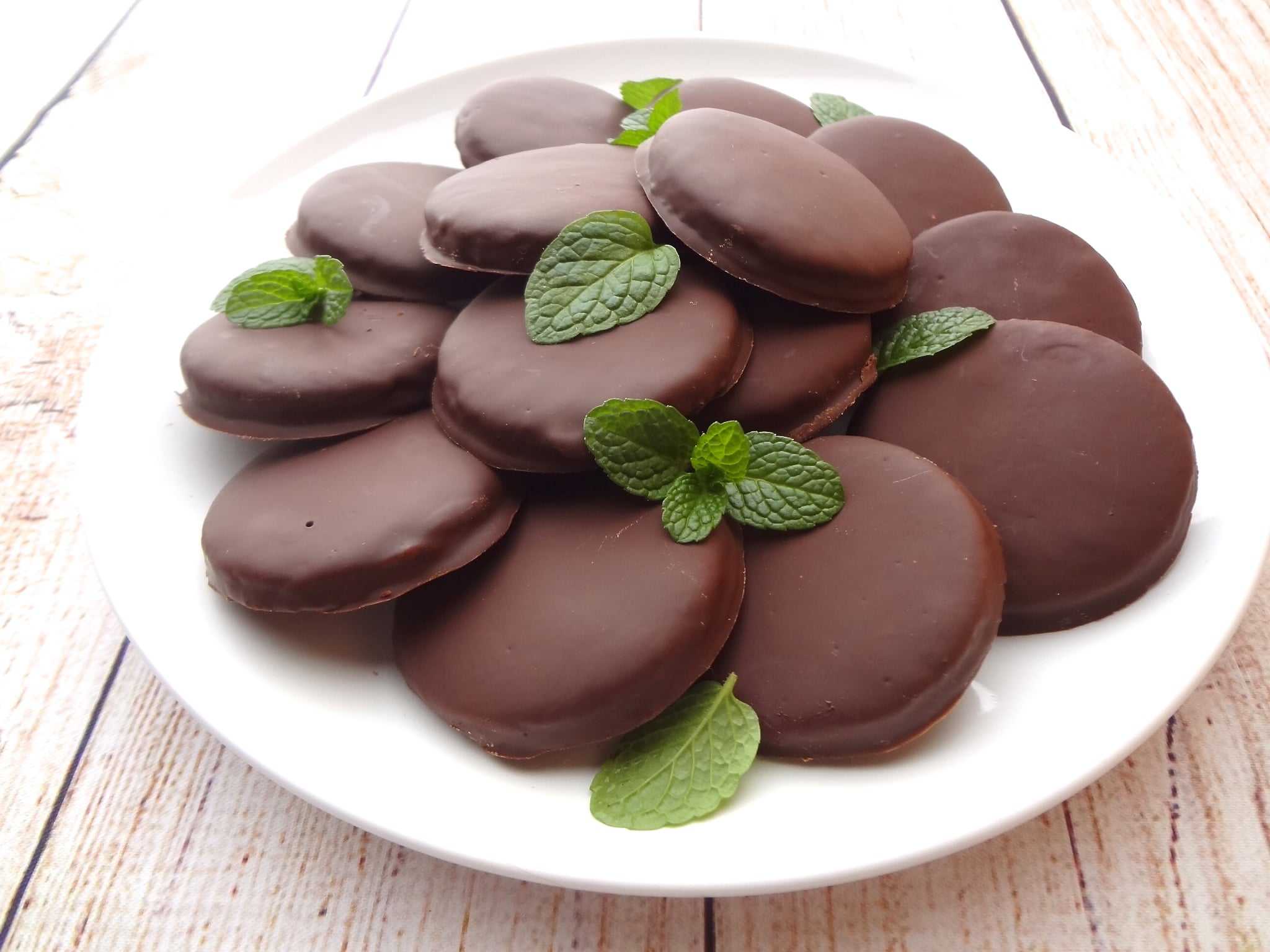 Vegan Thin Mints on a white plate and white wood with mint leaves.