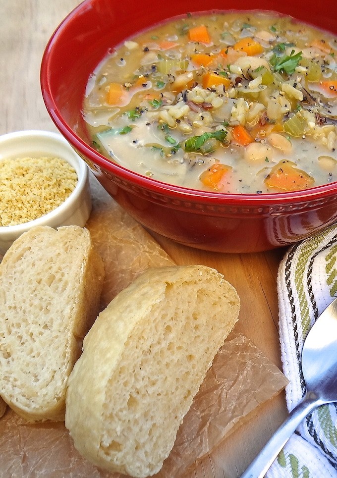 Quick One-Pot Veggie and Wild Rice Soup - vegan. A red bowl of veggie and wild rice soup loaded with white beans, chopped carrots & celery and diced onion then topped with fresh chopped parsley and black pepper. Served with a side of vegan cashew parmesan and fresh baked French bread slices.