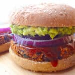 A vegan black bean burger topped with bbq sauce, rings of red onion, and mashed avocado.