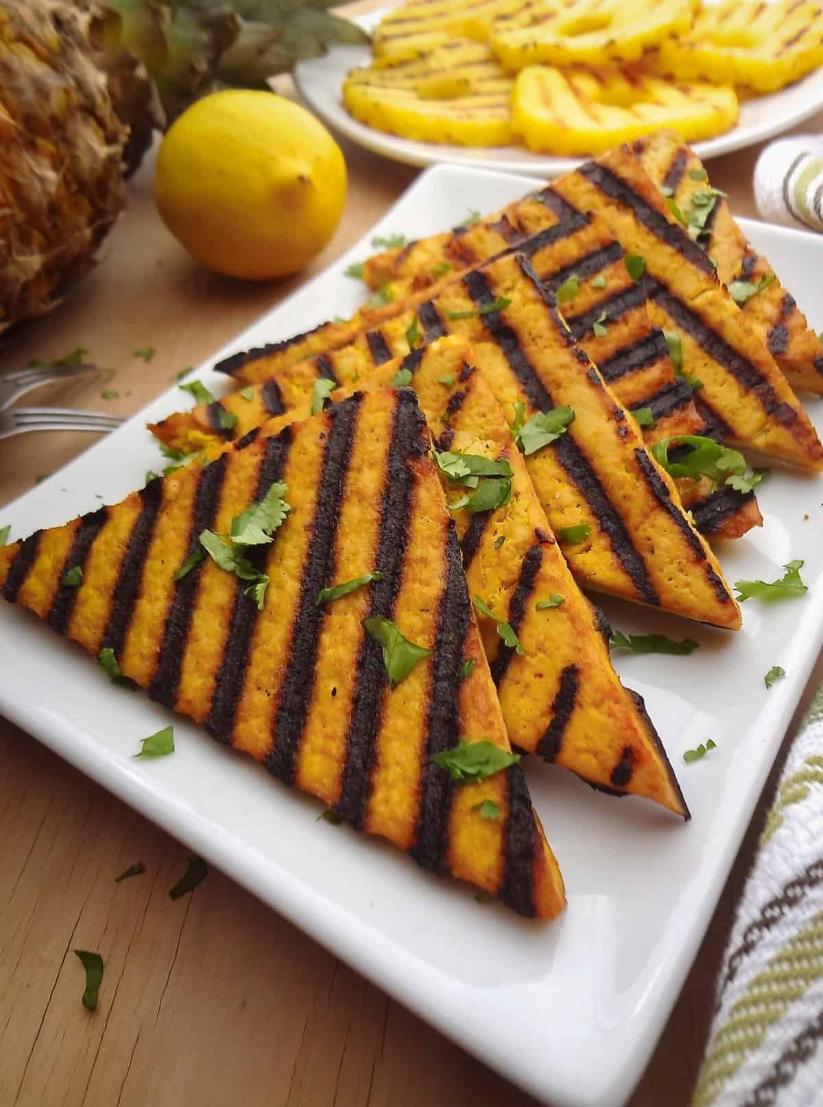 Six tofu slices with grill marks on a white plate topped with finely chopped cilantro.