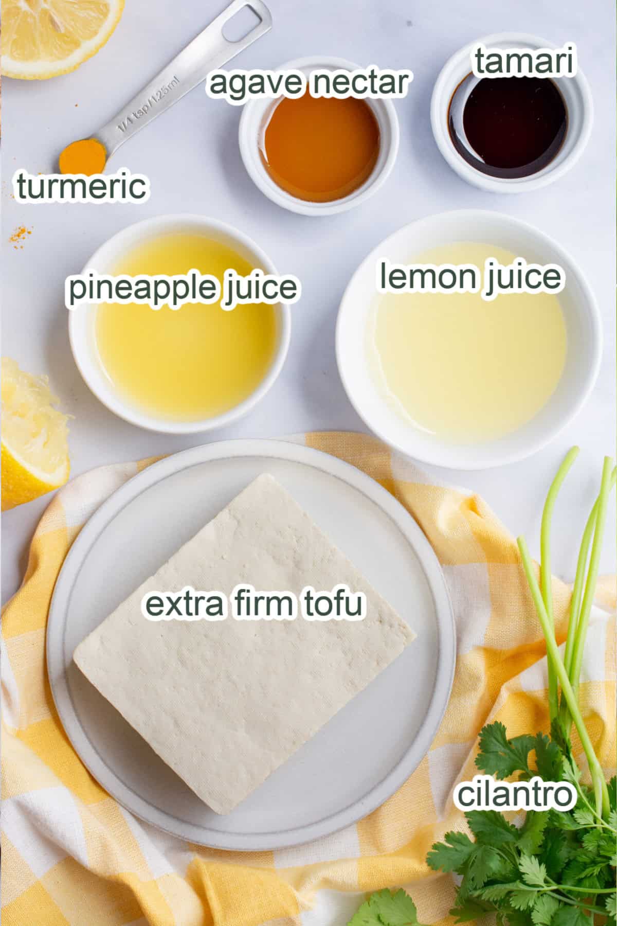 Recipe ingredients in separate bowls, a block of tofu, lemon juice, pineapple juice, agave nectar, tamari, turmeric, and fresh cilantro.