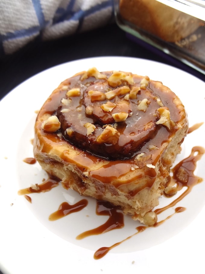 Refined sugar free vegan cinnamon roll topped with maple icing and chopped nuts.