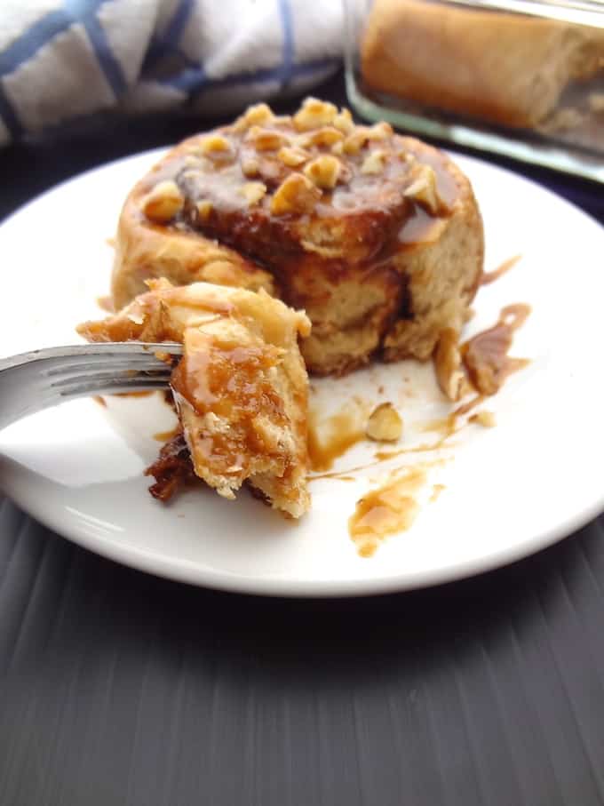 Vegan cinnamon roll on a white plate with a bite on a fork.