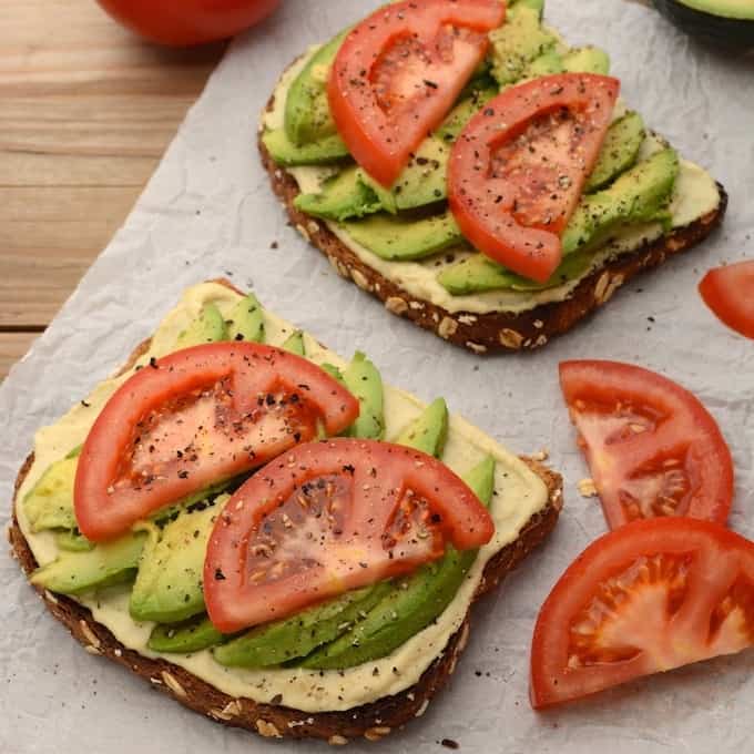 2 slices of hummus avocado toast topped with tomato slices.