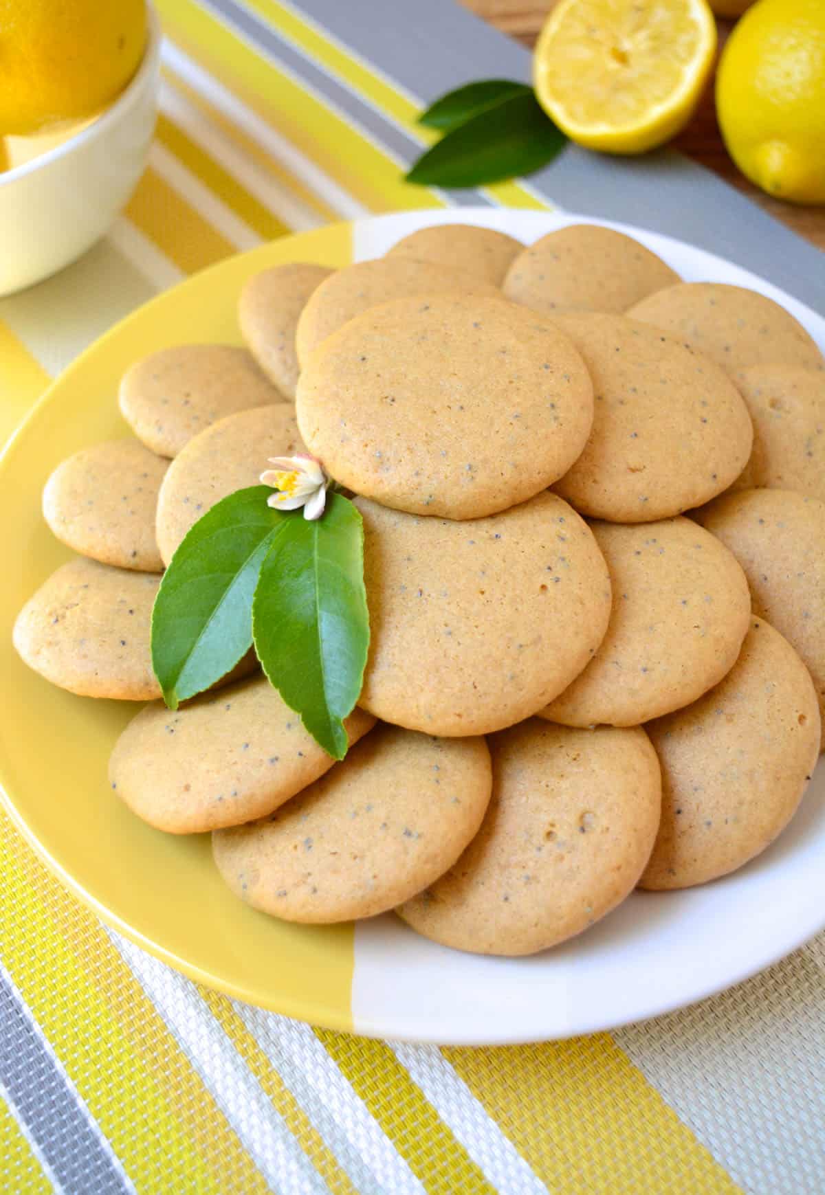 Vegan lemon cookies with poppy seeds stacked on a plate.