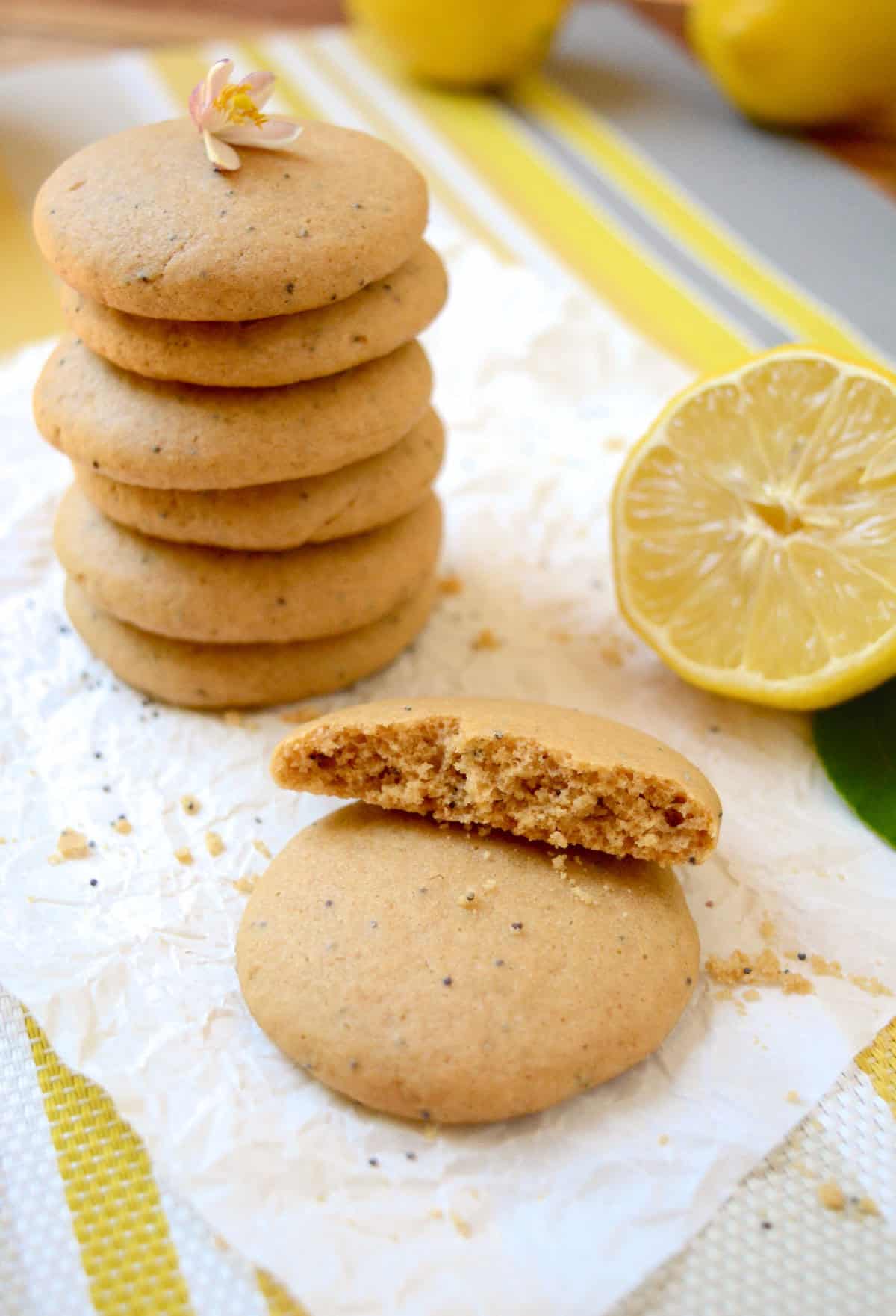 A stack of 6 vegan lemon cookies with a flower on top and a stack of 2 with one of the cookies broken in half.