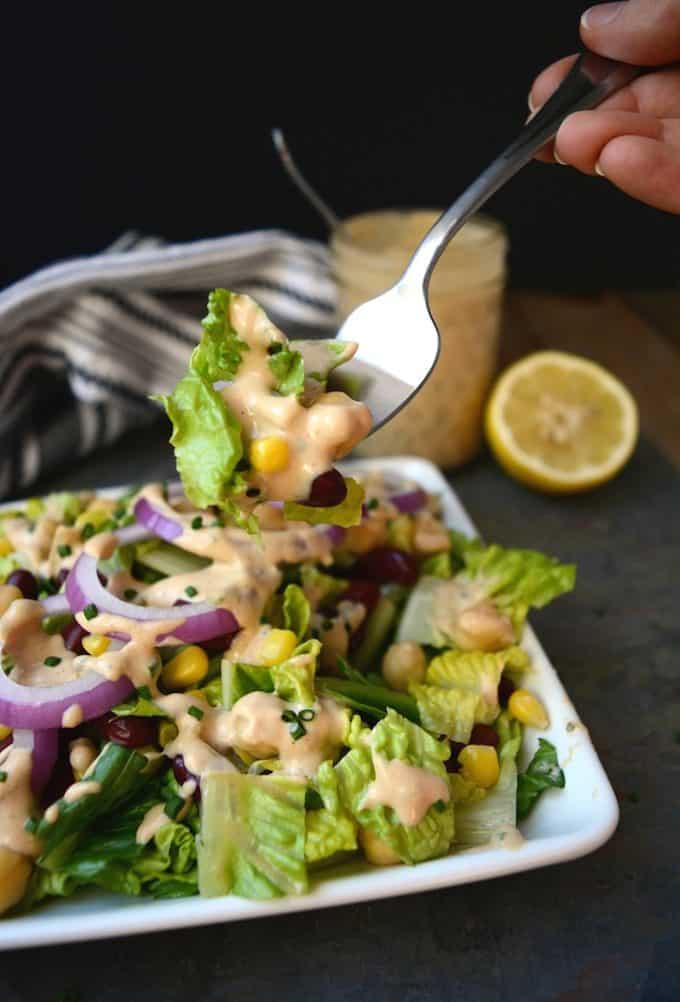 Salad topped with Creamy Vegan BBQ Ranch Dressing on a fork and jar of dressing in the background.