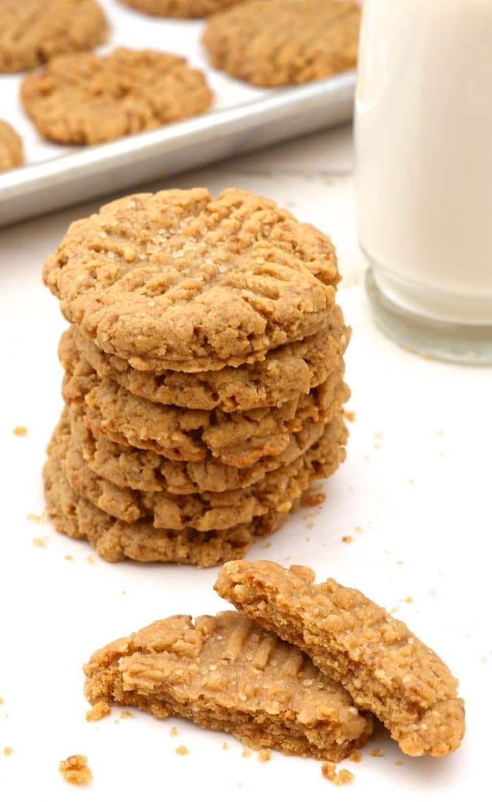 A stack of vegan peanut butter cookies and a glass of milk  and pan of cookies in the background.