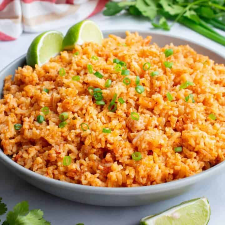 A serving bowl of Mexican rice with two lime wedges.