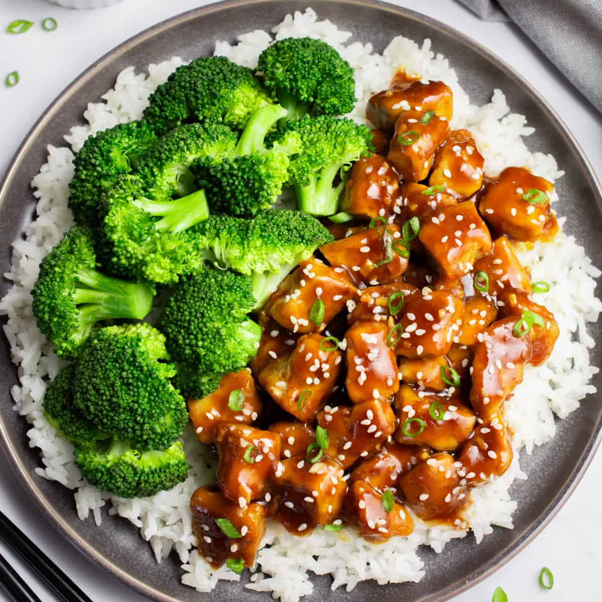 Overhead of a plate of white rice topped with vegan teriyaki tofu and steamed broccoli florets.