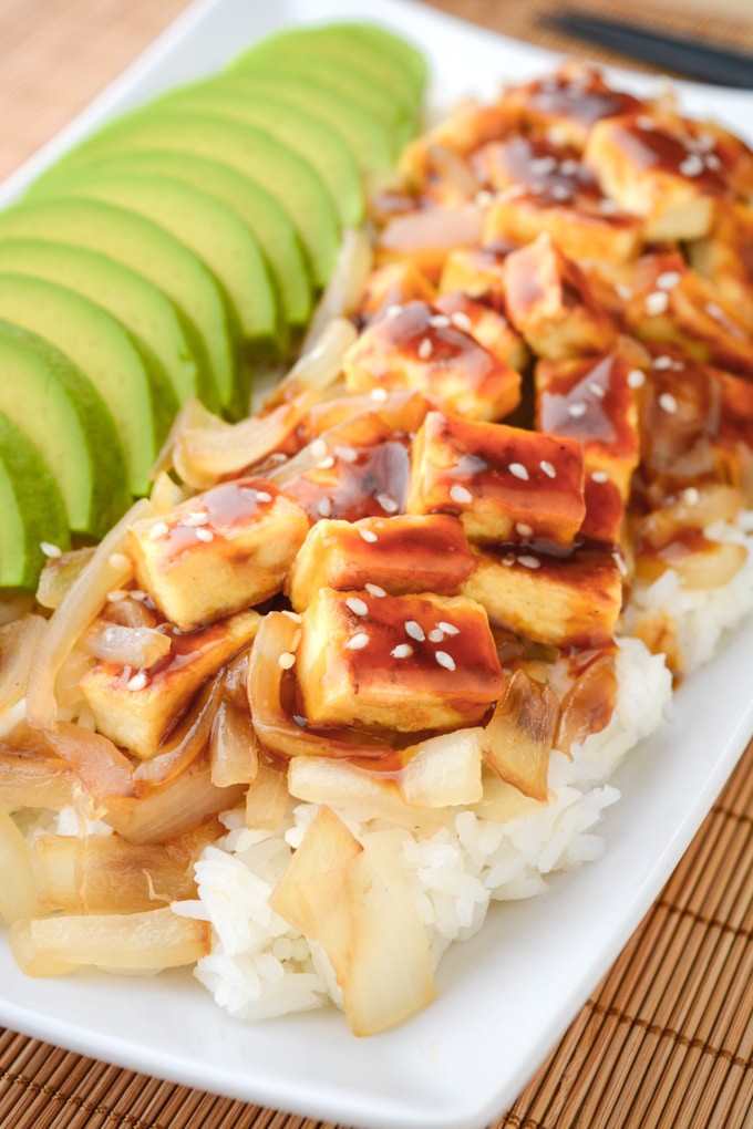 Teriyaki Tofu with sliced avocado and grilled onions on a bed of white basmati rice.