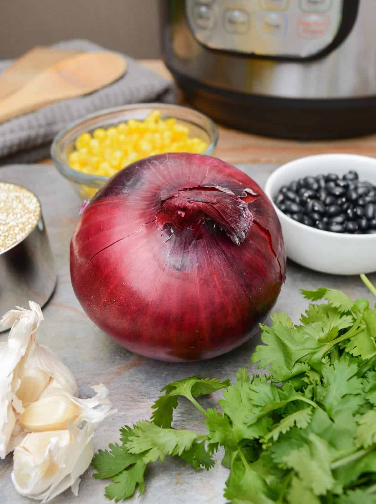 Whole food ingredients such as red onion, fresh cilantro, corn, black beans, dry quinoa, and garlic cloves. And an Instant Pot in the background.