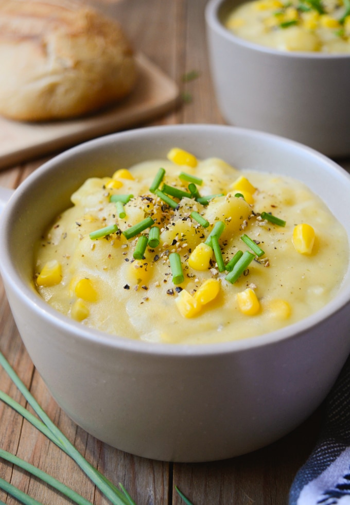 Vegan Potato Corn Chowder in a bowl topped with green onions and black pepper. Served with a sourdough bread loaf.