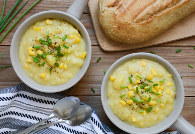 2 bowls of Vegan Potato Corn Chowder topped with green onions and fresh ground black pepper. Served with a sourdough bread loaf