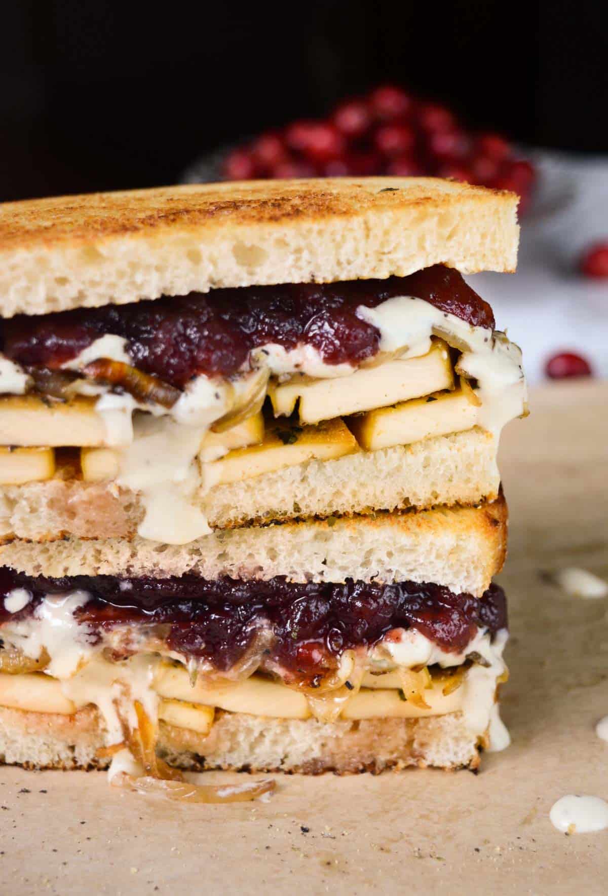 Vegan sandwich with tofu, dressing, onions, and cranberry sauce, cut in half and stacked.