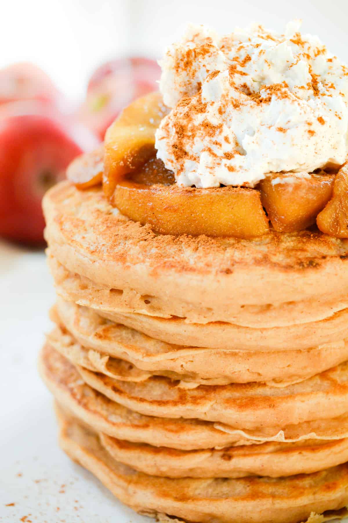 A fresh stack of vegan pancakes topped with cooked cinnamon apples and fluffy coconut whip.