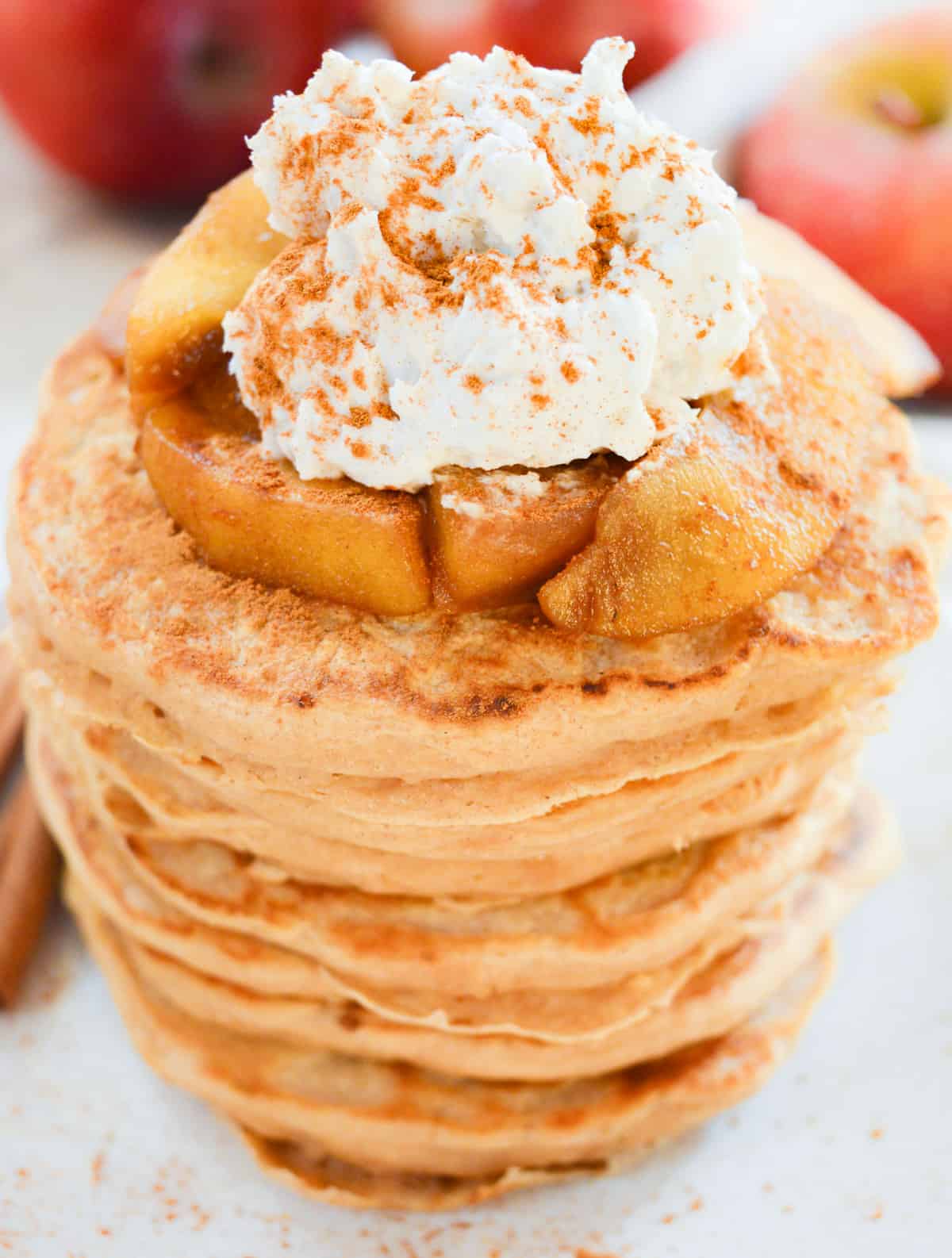 A large stack of vegan pancakes topped with cooked cinnamon apples and coconut whip.