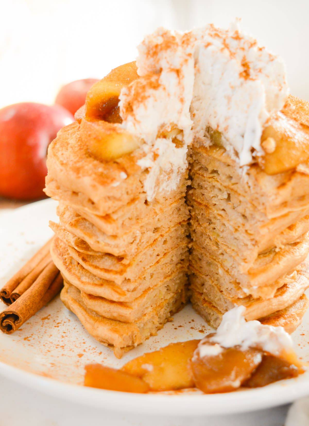 Vegan apple cinnamon pancakes with cooked apples and whipped cream on top and a bite removed.