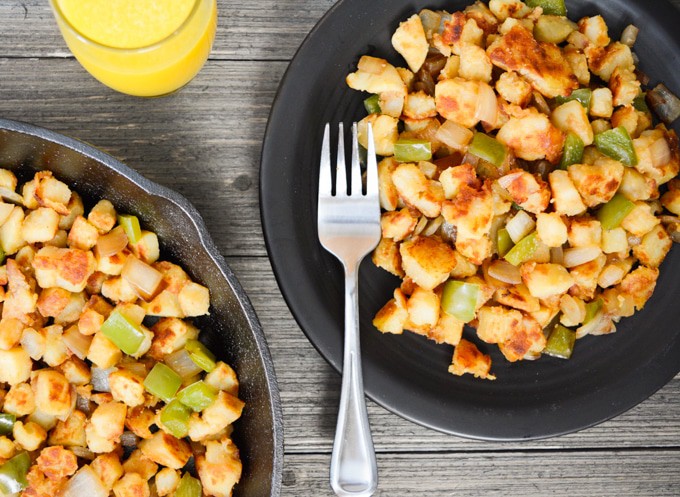 Top view of breakfast potatoes on a plate with fork and a glass of orange juice.