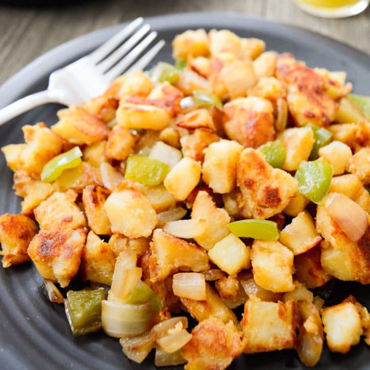 Sautéed breakfast potatoes with onions and bell peppers on a black plate.