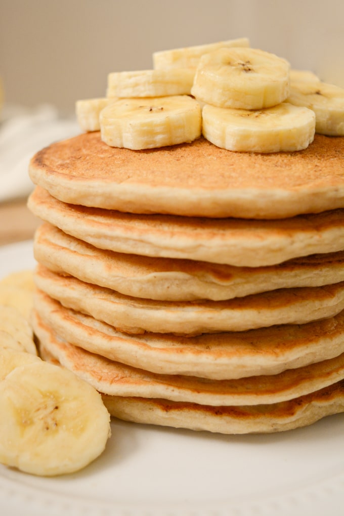 A stack of vegan banana milk pancakes topped with banana slices on a white plate.