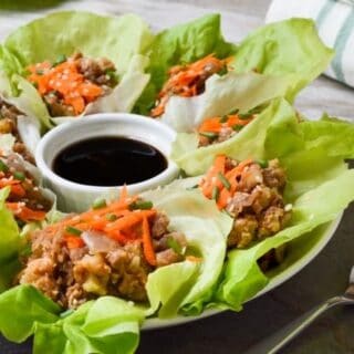 A plate of lentil-walnut filled lettuce wraps with a small white bowl of sesame sauce for dipping.