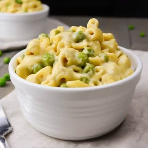 a white bowl filled with vegan macaroni and cheese with peas.