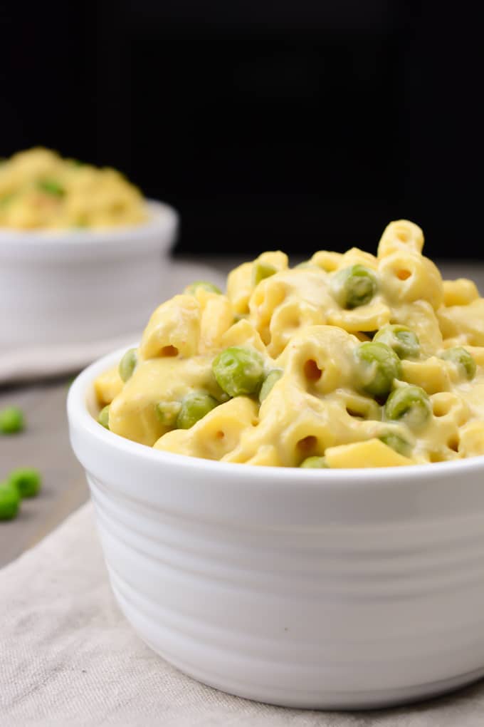 Creamy vegan mac and cheese with peas in a white bowl.