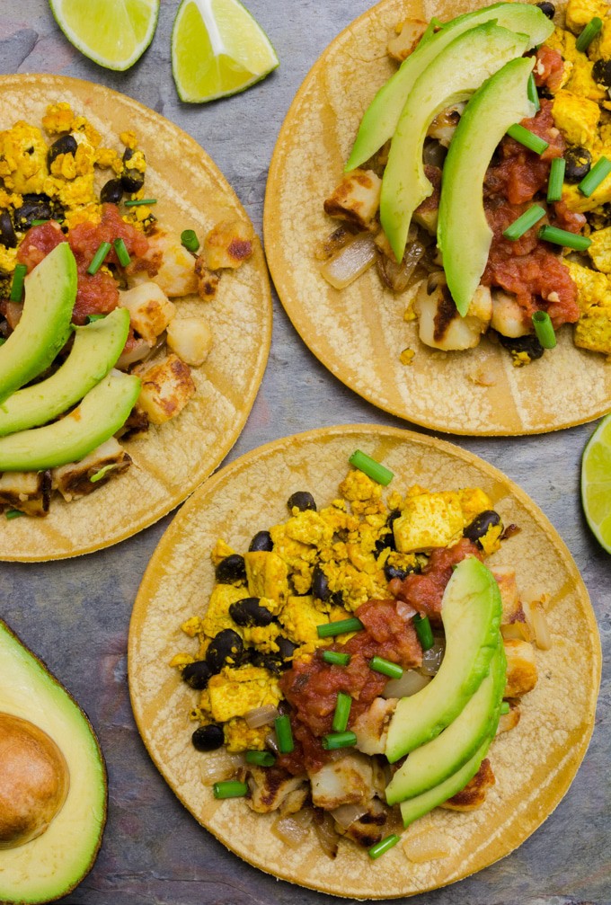 A top angle of 3 vegan breakfast tacos. there are a few cut lime wedges and half an avocado near by.