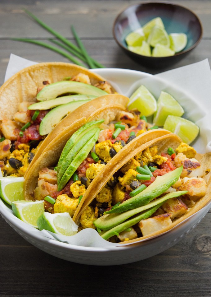 Vegan breakfast tacos in a white bowl with a small bowl of lime wedges. 