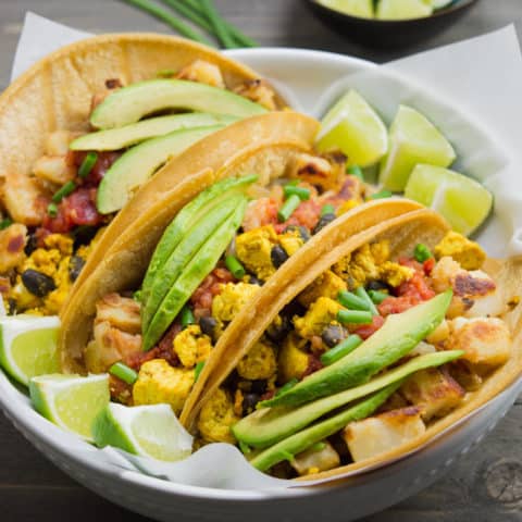 3 vegan breakfast tacos in a white bowl with lime wedges.