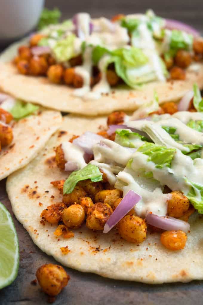 angle shot of chickpea soft tacos. 3 seasoned chickpeas on a homemade flour tortilla topped with lettuce onions and a cheesy vegan ranch.