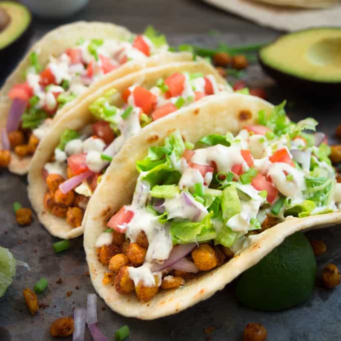 Three seasoned vegan chickpea tacos topped with ranch, lettuce, and tomatoes.