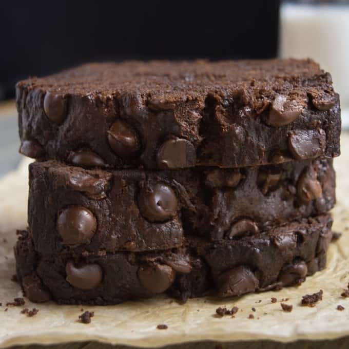 3 slices of vegan chocolate banana bread stacked with a cup of milk in the back.