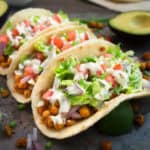 Three seasoned vegan chickpea tacos topped with ranch, lettuce, and tomatoes.