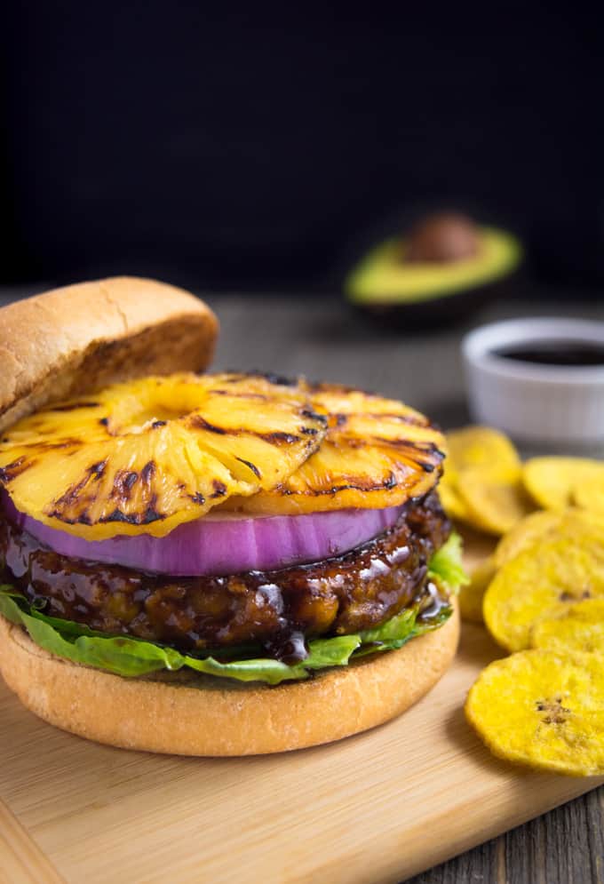 Grilled huli-huli vegan burger topped with red onion and grilled pineapple rings. It's served with a side of plantain chips.