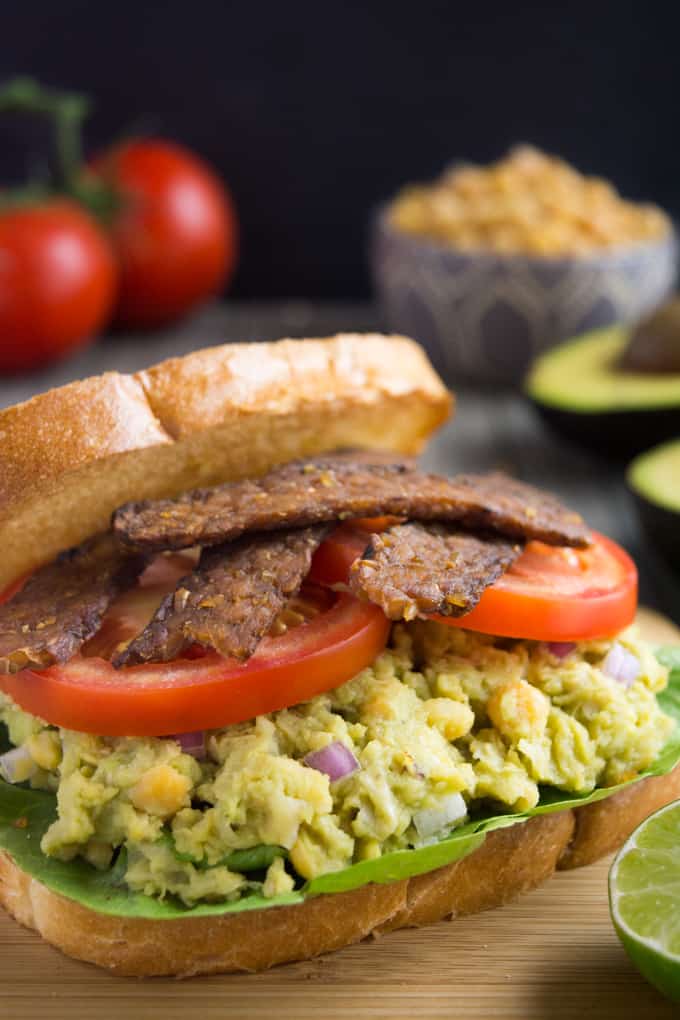 avocado chickpea BLT sandwich piled with lettuce, avocado chickpea mash, sliced tomato and tempeh bacon.