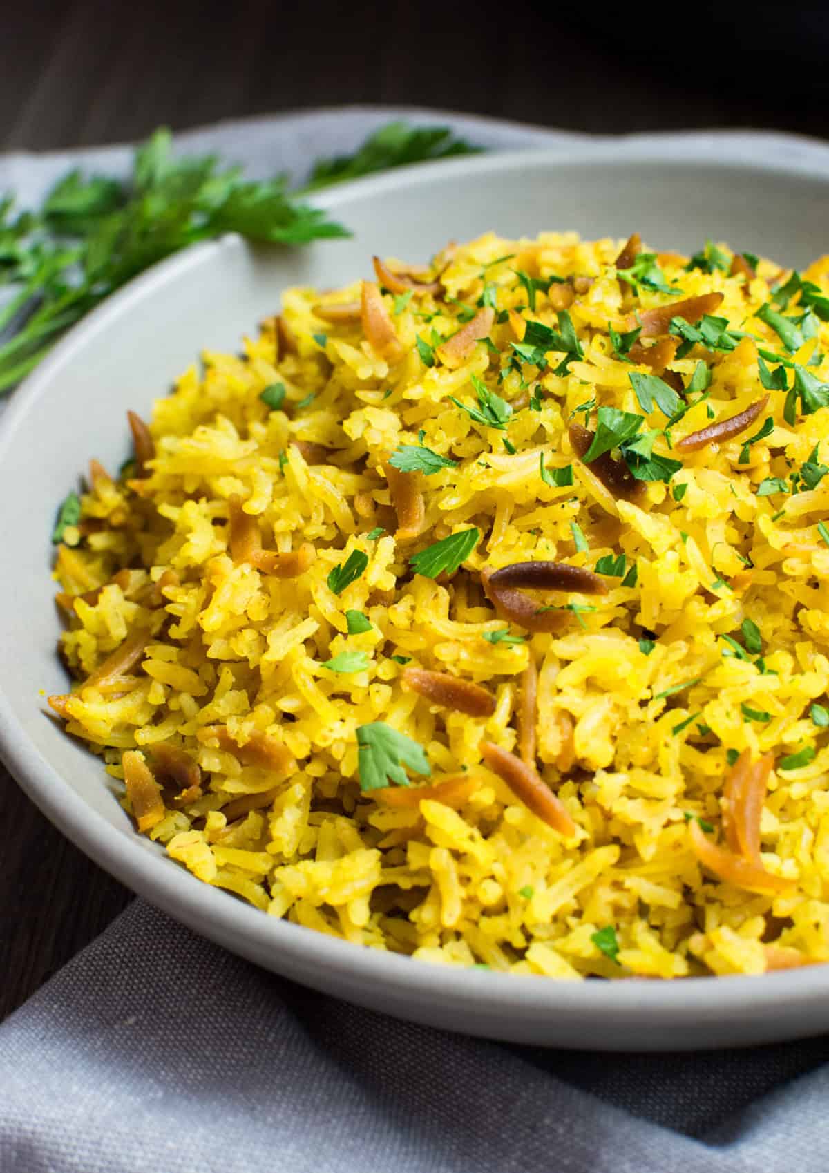 Yellow pilaf on a gray serving plate topped with chopped parsley.