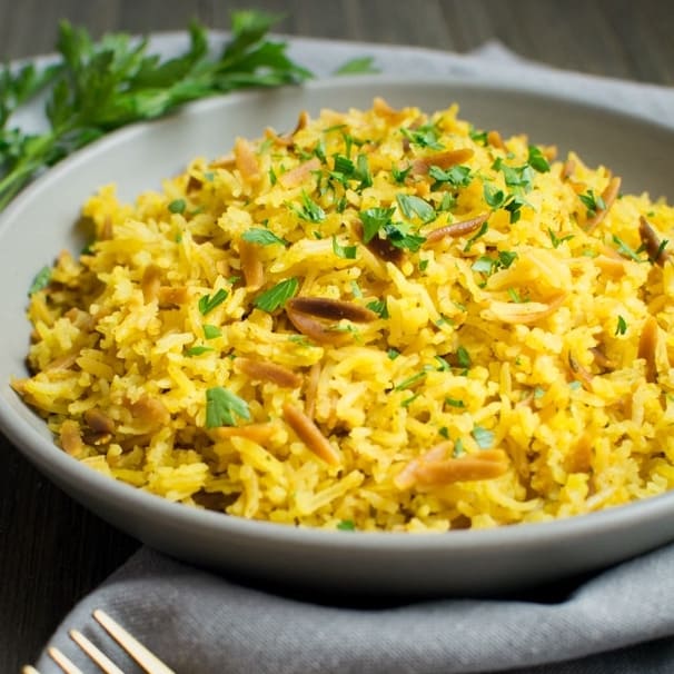 A gray bowl filled with rice pilaf topped with fresh chopped parsley.