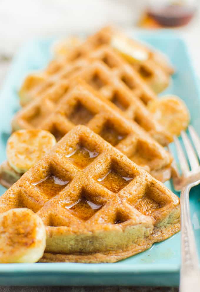 Cinnamon Vegan Waffles cut in triangles, topped with banana slices and drizzled with maple syrup.