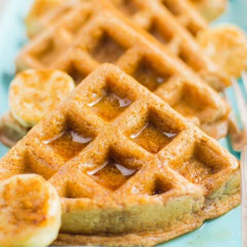 Vegan cinnamon waffle triangles topped with maple syrup on a rectangular turquoise plate.