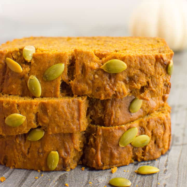 3 stacked slices of pumpkin bread topped with pumpkin seeds.